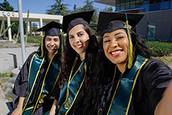 Three lady graduates in caps and gowns smiling.